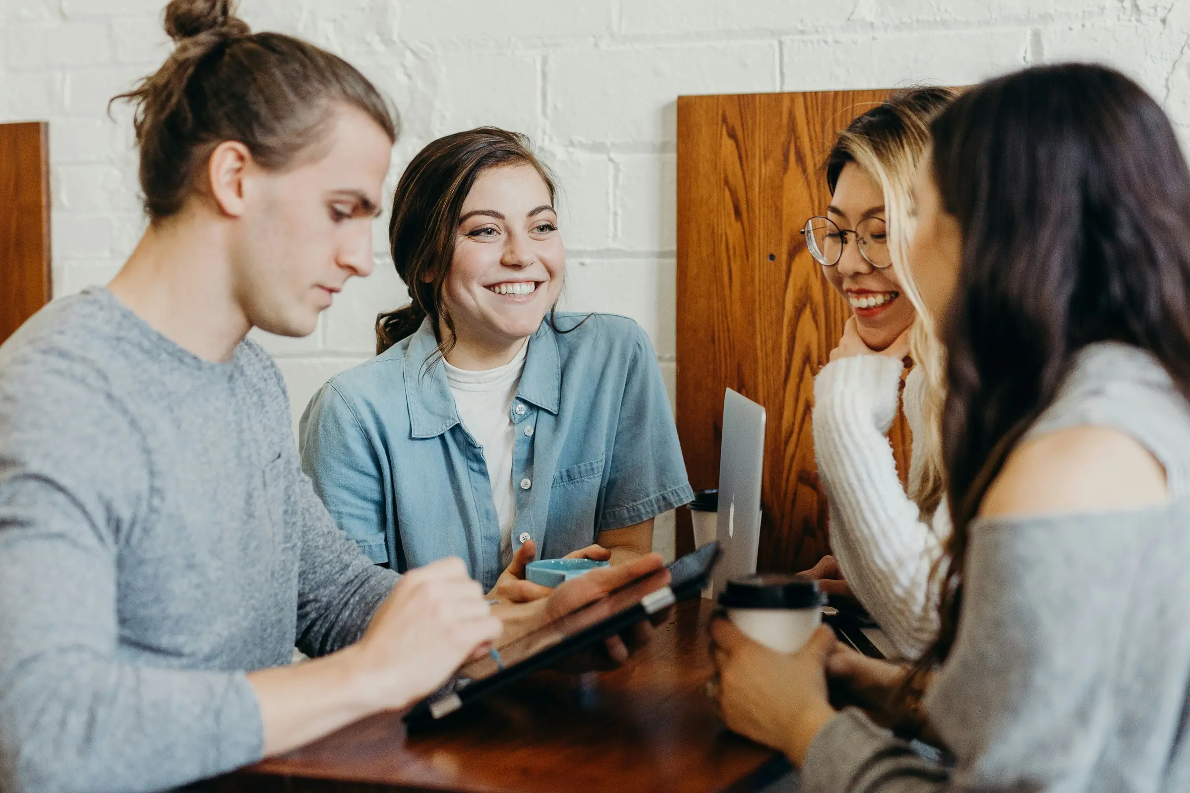 Four colleagues talking around a café table with a laptop and coffee